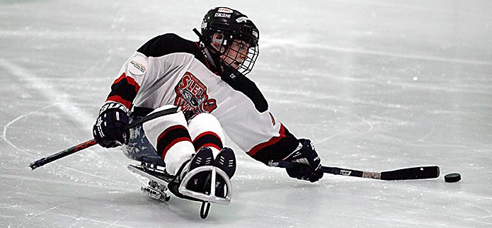 Joueur de para hockey sur sa luge, crosses en main